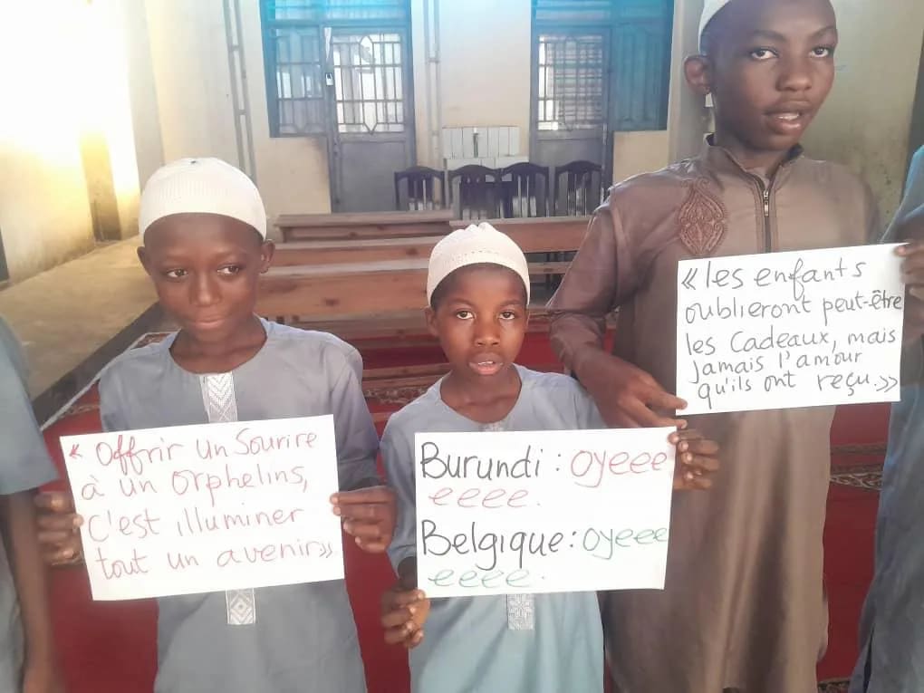 Trois garçons tiennent des pancartes écrites à la main : « Burundi : oyééé, Belgique : oyééé »