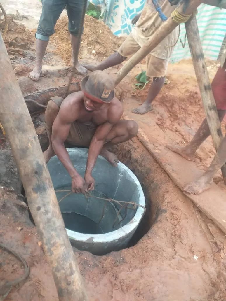 Un ouvrier au fond d'un puits en construction, au milieu des poutres de bois et de la terre rouge